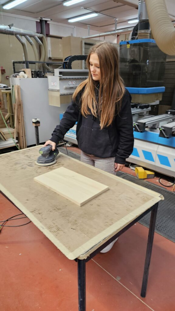 Une jeune fille en train de poncer un élément de van aménagé